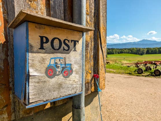Ein selbst gebauter Postkasten hängt an einem Bauernhof im ländlichen Raum. Das Motiv steht für Postzustellung, Briefversorgung und Infrastruktur auf dem Land sowie die Erreichbarkeit abgelegener Höfe.