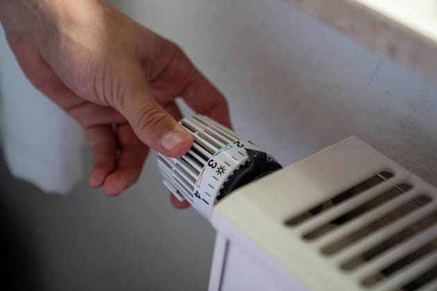 Eine Hand dreht den Thermostatregler an einem Heizkörper. Symbolbild zu den Themen Heizen, Heizkosten, Energieverbrauch und Energiesparen. Copyright: xSvenxHeidmannx