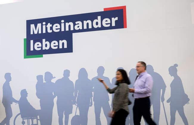 Feature, Slogan Miteinander Leben und den Schatten verschiedener Menschen, davor Besucher. REHACARE Fachmesse für Rehabilitation und Pflege, vom 23.09. - 26.09.2026 in Düsseldorf Deutschland. Messe