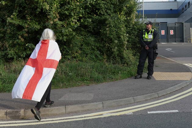 September 24, 2026, Basingstoke, Hampshire, UK: Basingstoke, UK. A woman draped in the flag of St George walks towards a police officer as members of The Patriot Platform and supporters Protest outside a police station where Daniel Thomas, also know as Danny Tommo, is being held, in Basingstoke, Hampshire. Anti-migrant protester Daniel Thomas has been arrested on suspicion of criminal damage with intent to endanger life after an incident in the English Channel. Basingstoke UK  - ZUMAl94_ 20260924_zaf_l94_037 Copyright: xJacquelinexLawriex