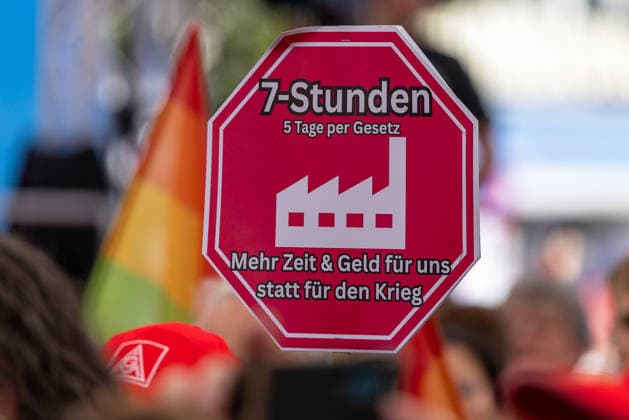 DGB Bayern - Hart verdient! Groß-Kundgebung, Nürnberg, 26.09.2026 Ein Demoschild mit der Aufschrift 7-Stunden, 5 Tage per Gesetz und dem Slogan Mehr Zeit & Geld für uns statt für den Krieg wird bei einer Kundgebung des DGB Bayern hochgehalten. Im Hintergrund sind weitere Teilnehmende mit Fahnen zu erkennen. Nürnberg Bayern Deutschland