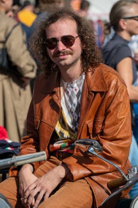 September 26, 2026, London, United Kingdom: An attendee at the King™s Cross Classic Car Boot Sale in London wears an orange leather jacket while sitting on a classic Italian scooter. The Kings Cross Classic Car Boot Sale returned to Granary Square and Stable Street, King™s Cross, London, for its 11th year. Held several times throughout the year, the event brings together vintage fashion, second-hand clothing, jewellery, homewares, collectables and vinyl records alongside classic cars, motorcycles and commercial vehicles. Visitors browsed stalls and traders, with many making a special effort to dress in period clothing inspired by the 1950s, 1960s and 1970s.continuing a tradition associated with the event. London United Kingdom - ZUMAs197 20260926_aaa_s197_379 Copyright: xJamesxWilloughbyx