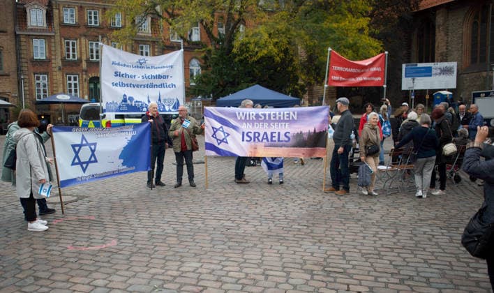Flensburg, Schleswig-Holstein Flensburg gedenkt den Opfern des 7. Oktober 2023. Hier: Personen entfalten Transparente mit farblich weiß-blauen Hintergrund. LInks: Judenstern und Text Gegen jeden Antisemitismus, immer und überall! Für Respekt, Menschlichkeit und Zusammenhalt. Mitte: Jüdisches Leben in Flensburg. Sicher - sichtbar - selbstverständlich. Rechts Wir stehen an der Seite Israels. Rechts außen (Transparent in Rot mit weißer Schrift) 7. Oktober 2023, Terroranschlag auf Israel. 1200 Ermordete, 250 Verschleppte.Aufnahme vom 07.10.2026, Flensburg