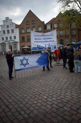 Flensburg, Schleswig-Holstein Flensburg gedenkt den Opfern des 7. Oktober 2023. Hier: Personen entfalten Transparente mit farblich weiß-blauen Hintergrund. LInks: Judenstern und Text Gegen jeden Antisemitismus, immer und überall! Für Respekt, Menschlichkeit und Zusammenhalt. Rechts: Jüdisches Leben in Flensburg. Sicher - sichtbar - selbstverständlich. Aufnahme vom 07.10.2026, Flensburg