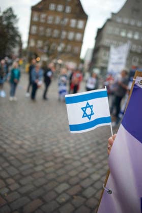 Flensburg, Schleswig-Holstein Flensburg gedenkt den Opfern des 7. Oktober 2023. Teilnehmer versammeln sich auf dem Südermarkt. Vorner Pserson hält Flagge von Israel. Es werden Lieder gesungen und die Namen und Geschichten einzelner Opfer des Terroranschlages vorgelesen. Aufnahme vom 07.10.2026, Flensburg