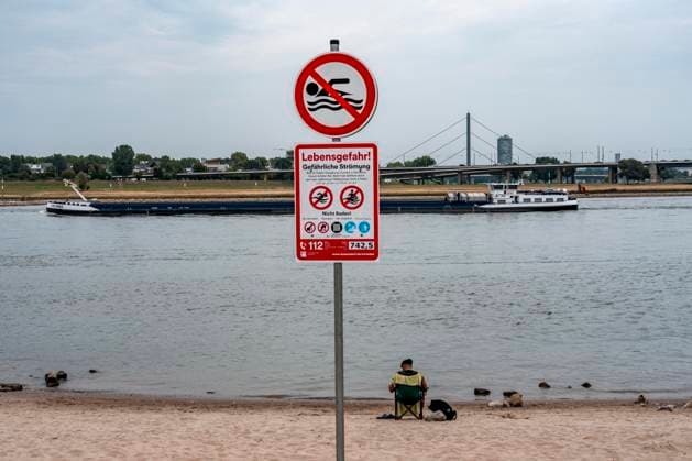 Erster Tag des Badeverbots im Rhein in Düsseldorf, nach 5 Todesfällen im Rhein, innerhalb von 12 Tagen nur in Düsseldorf, hier am beliebten Paradiesstrand, südlich der Innenstadt, sind nur wenige Besucher, trotz Temperaturen über 30°C, die meisten Leute gehen, wie erlaubt, nur noch bis zum Fussknöchel ins Wasser, doch immer noch gehen Menschen im Fluss schwimmen, auch Kinder, selbst wenn große Frachtschiffe, mit nur gut 30 Metern vom Ufer vorbei fahren, es drohen Bußgelder bis zu 1000€, Düsseldorf, NRW, Deutschland, Badeverbot Rhein