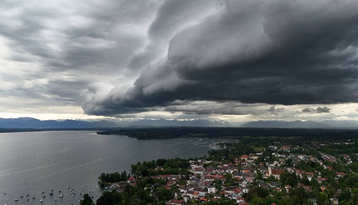 Ein Frühsommertag in Tutzing (Landkreis Starnberg). Hier der Blick über die Ortschaft und den Starnberger See mit der Alpenkette am Horizont, wo gerade ein Unwetter aufzieht, drüberzieht, eine Wolkenwand, Gewitterwalze, Wolkenrolle, Gewitterfront, Gewitterrolle, Unwetterfront, dunkle Wolken, Wetterbild