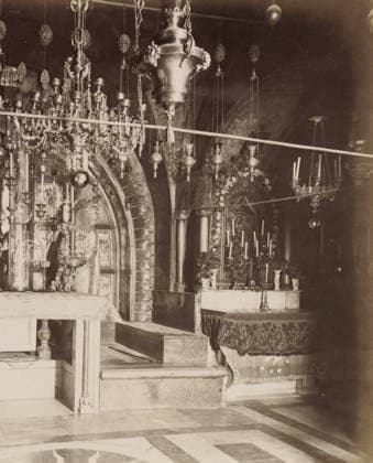 RECORD DATE NOT STATED XII et XIII Stations, le Calvaire, autel grec.- places., negative number: 270 , photographer: attributed to Maison Bonfils, Church of the Holy Sepulchre, c. 1867 - c. 1895, Jerusalem, Attributed to, pasteboard, paper, albumen print, height 224 mm x width 283 mm, altar, stations of the cross, Church of the Holy Sepulcher, A sepia-toned interior photograph showing an ornate religious space with hanging lamps and elaborate metal chandeliers suspended from the ceiling, a decorative archway with radiating carved elements, carved columns, candleholders with tall candles, an altar draped with patterned cloth, a statue or carved figure seated within a niche, floral garlands around a framed decorative panel, intricate metalwork and chains, stone st Copyright Penta Springs LCK260531_18267