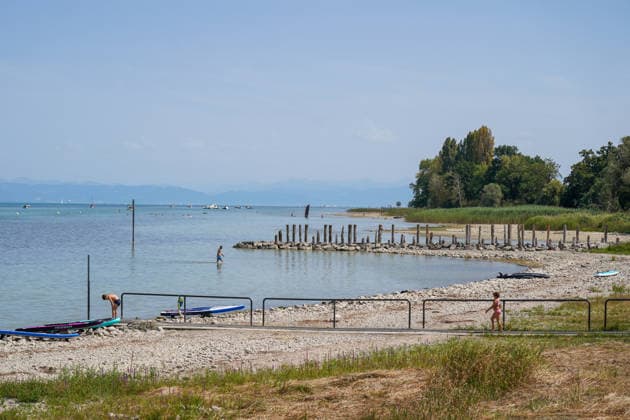 Schweiz, Bodensee: Niedriger Wasserstand legt breite Kies- und Uferflächen frei. Badegäste stehen im flachen Wasser, SUP-Boards liegen am Ufer; im Hintergrund Boote und Alpenpanorama. Symbolbild für Bodensee, Wasserstand, Niedrigwasser, Trockenheit, Hitze, Hitzewelle, Sommer, Klimawandel, Gewässer, Ufer, Kiesstrand, Baden, Abkühlung, Freizeit, Wassersport, Natur, Umwelt, Schweiz. Copyright: xJOERANxSTEINSIEKx