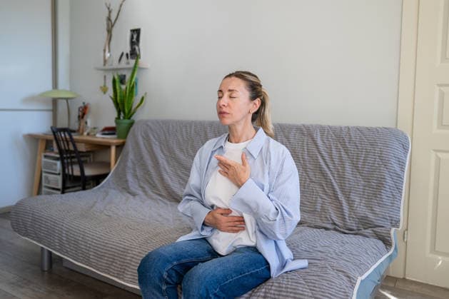 Eine positive, reife Frau, die zu Hause Selbsthilfetechniken zum Stressabbau und zur Tiefenatmung praktiziert. Calm mature woman do stress relief deep breathing self helping therapy, female sitting on sofa holding hands on chest inhaling air, focusing on physical and mental relaxation, healing zen practice (License=RF) ,model released, Symbolfoto Copyright: xZoonar.com DmitriixMarchenkox 25424105 ,model released, Symbolfoto ,property released