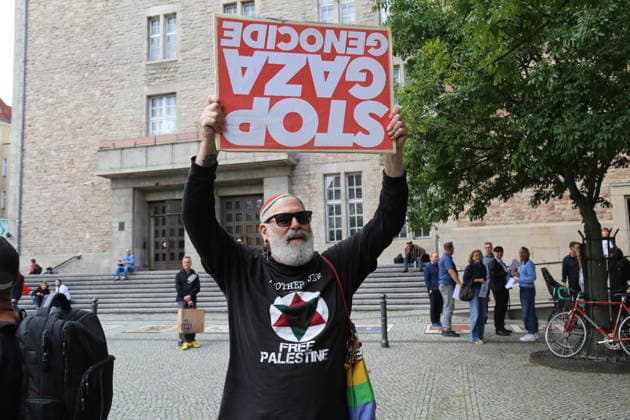 Berlin, Deutschland 17.09.2026: Ein pro-palästinensischer Demonstrant hält vor dem Rathaus Neukölln ein Plakat mit der Aufschrift STOP GAZA GENOCIDE. Im Hintergrund findet die Solidaritätsaktion Berlin trägt Davidstern statt. Protest, Demonstration, Gaza, Palästina, Israel, Nahostkonflikt, Gegenprotest, Meinungsfreiheit, Rathaus Neukölln, Solidarität, jüdische Gemeinschaft. Copyright: xAlonxDavidx