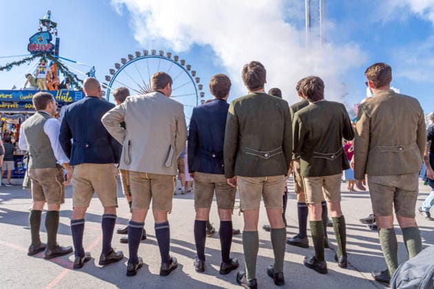 Oktoberfest 2026, Wiesn-Start bei strahlendem Sonnenschein und Temperaturen bis 24 Grad, bestes Wiesnwetter, Touristen aus den USA in bayerischer Tracht vor dem Riesenrad, Eröffnungstag, 19. September 2026 Deutschland, München, 19. September 2026, Oktoberfest 2026, Wieesn-Start bei strahlendem Sonnenschein und Temperaturen bis 24 Grad, eine Gruppe von US-Touristen Touristen stilecht in bayerischer Tracht vor dem Riesenrad, Deko-Nebel vom Fahrgeschäft Hangover, mittags um 12:30 kurz nach der Eröffnung, blauer Himmel, bestes Wiesnwetter, typisch bayerisch, Volksfest, Bayern,