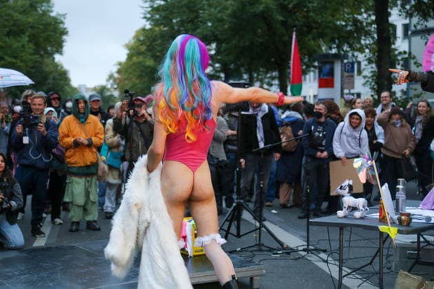 Berlin, Deutschland 24.09.2026: Performance bei der Protestkundgebung gegen die Verleihung des Axel Springer Awards an Peter Thiel. Eine leicht bekleidete Person mit regenbogenfarbener Perücke tritt vor Demonstranten auf, im Hintergrund eine Palästina-Fahne. Demonstration, Protest, Performance, Peter Thiel, Palantir, Axel Springer Award, Palästina, Regenbogen, LGBTQ, Queer, Aktivismus, Kundgebung, Publikum. Copyright: xAlonxDavidx