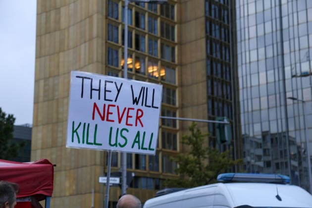 Berlin, Deutschland 24.09.2026: Protestplakat mit der Aufschrift THEY WILL NEVER KILL US ALL vor dem Axel-Springer-Hochhaus während der Kundgebung gegen die Verleihung des Axel Springer Awards an Peter Thiel. Im Vordergrund ein Polizeifahrzeug. Demonstration, Protest, Peter Thiel, Palantir, Axel Springer, Protestplakat, Transparent, Polizei, Polizeieinsatz, Sicherheit, Palästina, Nahost, Aktivismus, Kundgebung. Copyright: xAlonxDavidx