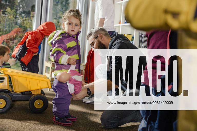 Pre-school teacher helping girl putting on rainwear in kindergarten model released Symbolfoto property released MFF04109