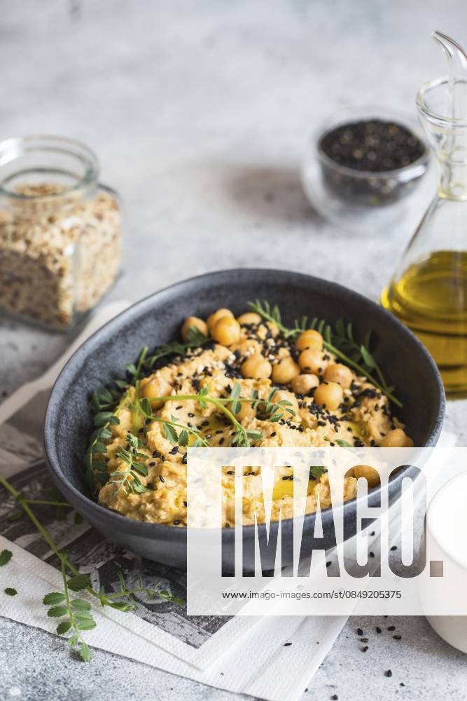 Kichererbsenhummus in der schwarzen Schale, dekoriert mit Sesamsamen und Kichererbsengrün. Vegane Rezepte, Gerichte auf pflanzlicher Basis. Konzept für umweltfreundliches Wohnen. Biologische Lebensmittel. Vegetarische Küche Chickpeas hummus in the black bowl decorated with sesame seeds and chickpeas greens. Vegan recipes, plant-based dishes. Green living concept. Organic food. Vegetarian cuisine