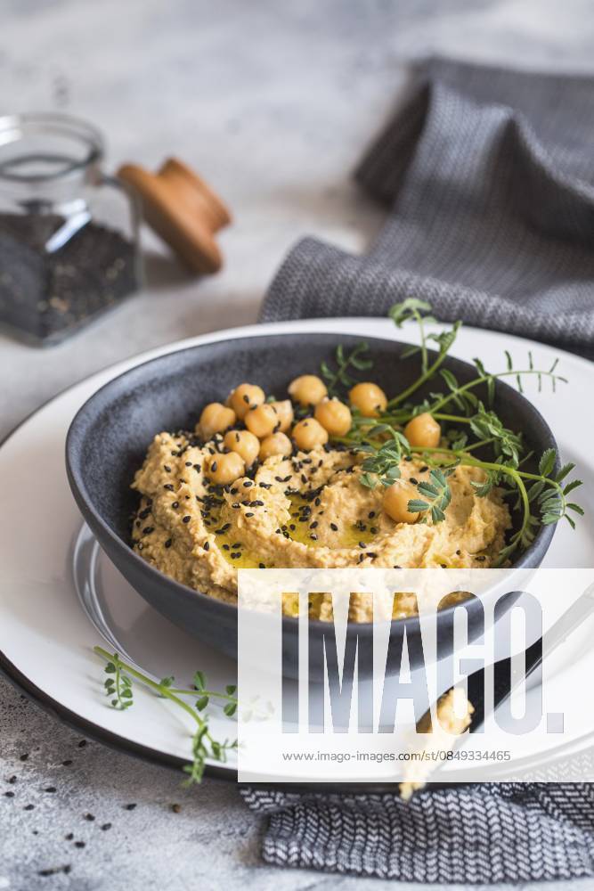 Kichererbsenhummus in der schwarzen Schale, dekoriert mit Sesamsamen und Kichererbsengrün. Vegane Rezepte, Gerichte auf pflanzlicher Basis. Konzept für umweltfreundliches Wohnen. Biologische Lebensmittel. Vegetarische Küche Chickpeas hummus in the black bowl decorated with sesame seeds and chickpeas greens. Vegan recipes, plant-based dishes. Green living concept. Organic food. Vegetarian cuisine