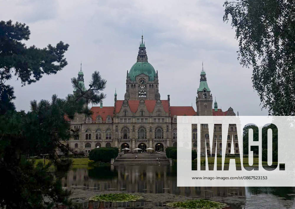 Hannover, Niedersachsen, Deutschland, Europa. Das Neue Rathaus von Hannover spiegelt sich im Maschteich. Die historische Rathausfassade mit ihrer markanten Kuppel und den Türmen ist von Parkanlagen und Bäumen eingerahmt. Im Vordergrund befindet sich der Teich mit Wasserpflanzen und Spiegelungen. Dokumentarische Aufnahme eines bekannten Wahrzeichens der Landeshauptstadt Hannover.