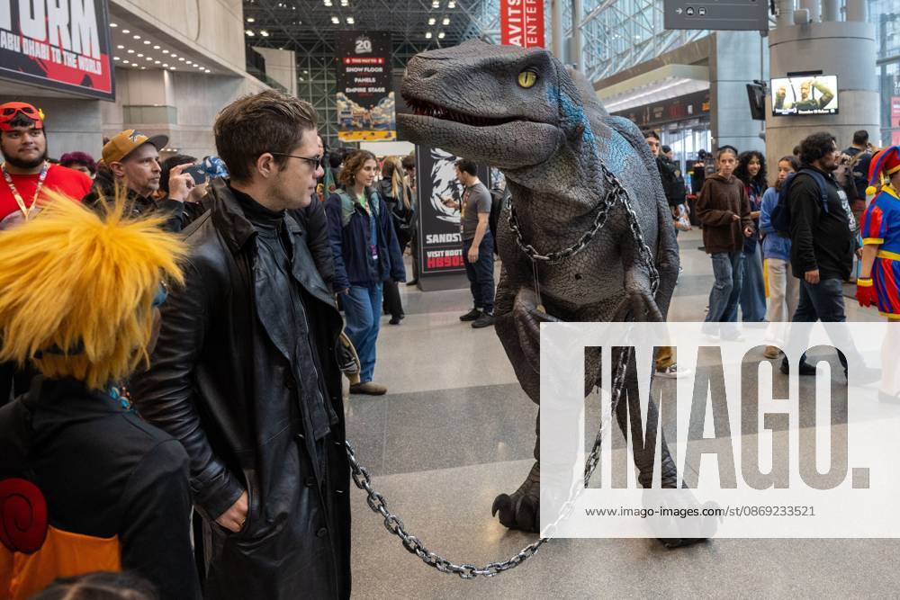 A cosplayer dressed in a long black leather coat and dark sunglasses posing alongside a person in a realistic animatronic Velociraptor costume (resembling Blue from Jurassic World).during New York Comic Con 2026 at The Jacob K. Javits Convention Center on October 11, 2026 in New York City. New York United States - ZUMAs197 20261011_aaa_s197_358