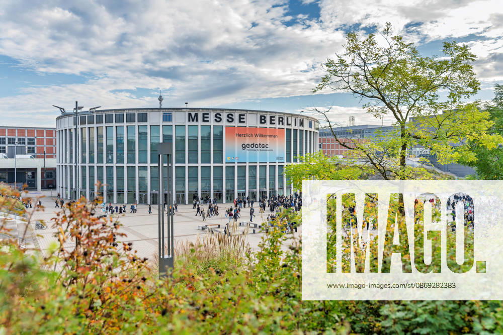Berlin, 13.10.2026: Herbstlich gefärbte Sträucher und Bäume rahmen den Rundbau am Eingang Süd der Messe Berlin, vor dem sich Besucher der gedatec sammeln; an der Fassade wirbt ein großes Banner für die neue Fachmesse für Gebäudetechnik. Die gedatec, Fachmesse für Gebäudetechnik, findet vom 13. bis 15. Oktober 2026 erstmals auf dem Berliner Messegelände statt und geht aus der Elektrotechnik-Fachmesse belektro hervor. Unter einer Dachmarke bündelt sie Elektrotechnik, Sanitär-, Heizungs- und Klimatechnik sowie das Dachdeckerhandwerk und richtet sich an Fachbesucher aus Handwerk, Planung und Industrie. Herbststimmung am Eingang Süd der Messe Berlin
