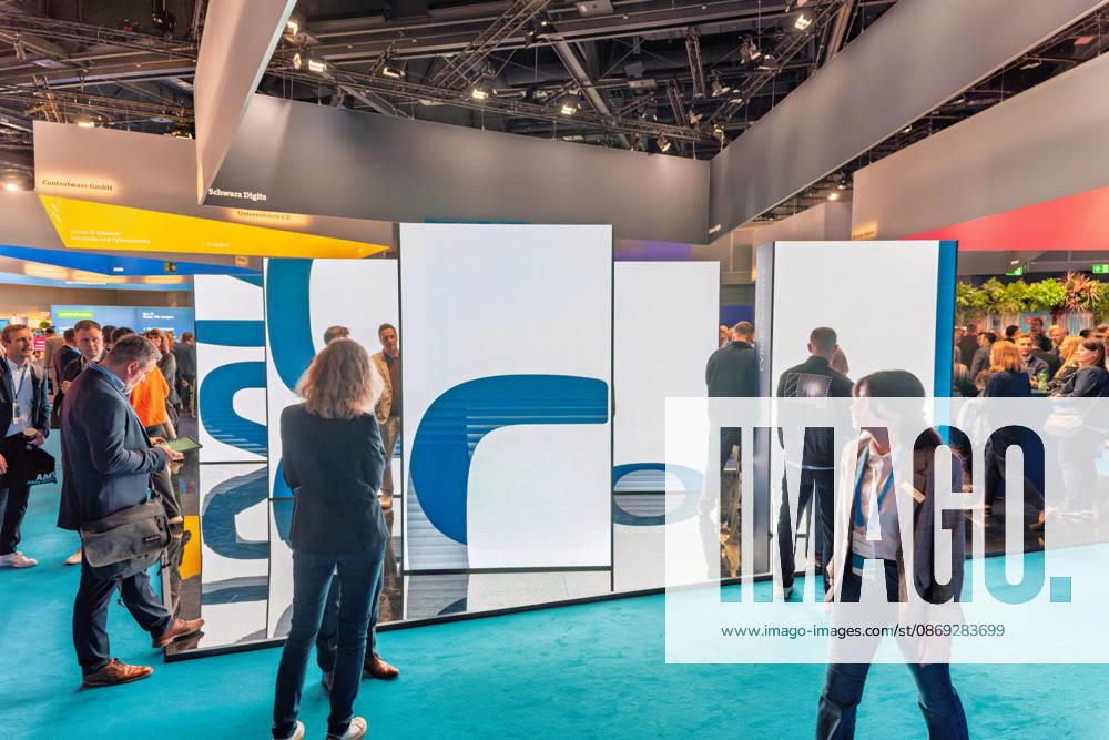 Berlin, 13.10.2026: Besucher gehen an einer großen LED-Installation im Ausstellungsbereich der Smart Country Convention in der Halle hub27 vorbei; darüber hängen die Standbanner von Schwarz Digits, Controlware und Rohde & Schwarz Networks and Cybersecurity. Schwarz Digits ist die IT- und Digitalsparte der Schwarz Gruppe (Lidl, Kaufland) und bietet mit STACKIT eine Cloud an, die als souveräne europäische Alternative für Verwaltungen und Unternehmen vermarktet wird. Die Smart Country Convention (SCCON) ist die Kongressmesse für die Digitalisierung des öffentlichen Sektors und wird vom Digitalverband Bitkom gemeinsam mit der Messe Berlin veranstaltet. Vom 13. bis 15. Oktober 2026 treffen sich in der Halle hub27 Vertreter aus Bund, Län