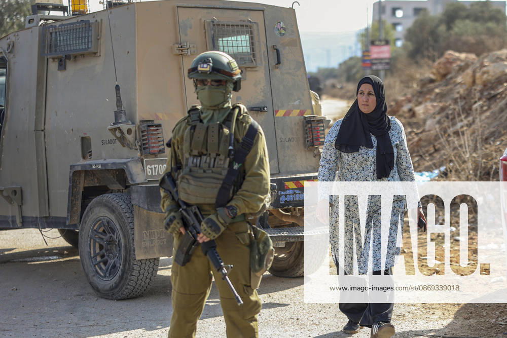 Settlers Disrupt Turmus Ayya Harvest An armed Israeli soldier stands beside a tan armored vehicle as a woman wearing a black headscarf walks nearby in Turmus Ayya, near Ramallah, in the Israeli-occupied West Bank, on October 13, 2026. Palestinian news agency WAFA, citing local sources, reported that Israeli settlers attacked the town and tried to prevent residents from reaching their land to harvest olives. Ramallah West Bank Palestinian Territories