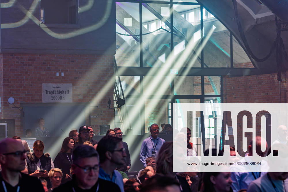 Berlin, 16.10.2026: Teilnehmerinnen und Teilnehmer der NeulandPro Connect 2026 verfolgen das Programm in der Backsteinhalle des WECC; Lichtstrahlen fallen durch den Nebel, ein altes Schild mit der Aufschrift Tragfähigkeit 2000 Kg erinnert an die frühere Nutzung des Gebäudes als Lagerhaus. Die zweitägige KI-Konferenz NeulandPro Connect 2026 findet am 16. und 17. Oktober im Westhafen Event & Convention Center (WECC) in Moabit statt, einem historischen Speichergebäude am Berliner Westhafen. Mit mehr als 50 Speakern sowie über 30 Workshops, Masterclasses und einem Hackathon richtet sich die Veranstaltung an Gründer, Führungskräfte, Unternehmen und KI-Interessierte. NeulandPro Connect 2026 - KI-Konferenz in Berlin