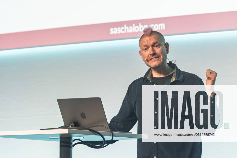 Berlin, 16.10.2026: Auf der NeulandPro Connect 2026 ballt der Publizist und Digital-Vordenker Sascha Lobo während seines Vortrags am Rednerpult die Faust. Die zweitägige KI-Konferenz NeulandPro Connect 2026 findet am 16. und 17. Oktober im Westhafen Event & Convention Center (WECC) in Moabit statt, einem historischen Speichergebäude am Berliner Westhafen. Veranstalter ist NeulandPro, eine Bildungs- und Medienmarke rund um Künstliche Intelligenz. Mit Vorträgen, Workshops und Hackathons richtet sich die Konferenz vor allem an kleine und mittelständische Unternehmen, Gründer und Führungskräfte, die KI praktisch einsetzen wollen; erwartet werden bis zu 1.000 Gäste. NeulandPro Connect 2026 - KI-Konferenz in Berlin