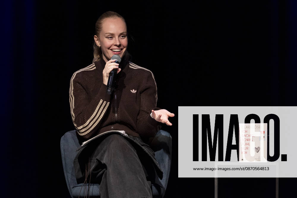 Poetry Artist, Autorin Clara LOESEL (LÖSEL) spricht laechelnd zum Publikum, bei ihrer Lesung, Previewshow zu ihrem neuen Buch ,Ich dachte, sowas fuehl nur ich, sitzend, mit Mikrofon, Einzelbild, Einzelfoto, im Theater am Tanzbrunnen, Koeln, am 23.10.2026.