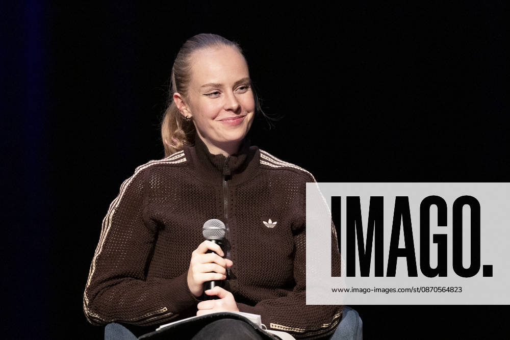 Poetry Artist, Autorin Clara LOESEL (LÖSEL) laechelnd, bei ihrer Lesung, Previewshow zu ihrem neuen Buch ,Ich dachte, sowas fuehl nur ich, sitzend, mit Mikrofon, Einzelbild, Einzelfoto, im Theater am Tanzbrunnen, Koeln, am 23.10.2026.