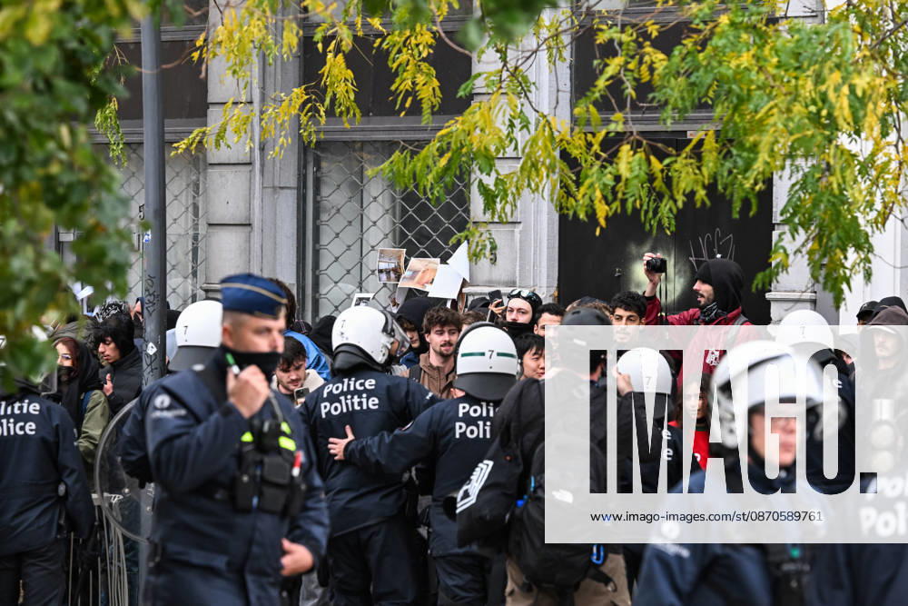 Riot police officers in protective gear surround a group of demonstrators, some wearing face coverings and others unmasked, during student protests in central Brussels, Belgium, on 24 October 2026. Several people film the police operation with their mobile phones as officers confront the protesters amid unrest in the city centre.