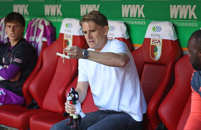 Fussball, Herren, Saison 2025 2026, FC Augsburg - FC Bayern München, Bundesliga, WWK Arena Christoph Freund, Sportdirektor (FC Bayern München) mit dem Gastgebergeschenk aus der Augsburger Puppenkiste, Kater Mikesch DFL DFB regulations prohibit any use of photographs as image sequences and or quasi-video