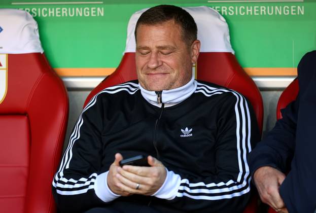 Fussball, Herren, Saison 2025 2026, FC Augsburg - FC Bayern München, Bundesliga, WWK Arena Max Eberl, Sportvorstand (FC Bayern München) sitzend auf der Trainerbank mit Blick auf das Handy, Smartphone, Telefon, grinsen, schmunzelnd DFL DFB regulations prohibit any use of photographs as image sequences and or quasi-video
