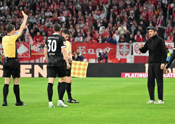 12.04.2026, xsltx, Fussball 1.Bundesliga, FSV Mainz 05 - SC Freiburg v.l. Felix Zwayer (Schiedsrichter) zeigt Julian Schuster (Cheftrainer SC Freiburg re.) wg. Reklamierens mit dem Pausenpfiff die gelbe Karte (DFL DFB REGULATIONS PROHIBIT ANY USE OF PHOTOGRAPHS as IMAGE SEQUENCES and or QUASI-VIDEO)