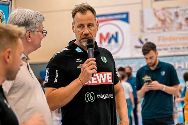 Maik Machulla, Offizieller der Rhein Neckar Löwen, spricht beim DHB-Pokal-Spiel zwischen Rein Neckar Löwen und SV Salamander Kornwestheim am 21.08.2026 in der Sporthalle Ost Kornwestheim ins Mikrofon. Der Funktionär trägt das schwarze Vereins-Outfit mit Sponsorenlogos (SAP, REWE, nagaro) und adressiert die anwesenden Zuschauer und Mannschaftsmitglieder. Maik Machulla spricht bei DHB-Pokal-Event in Kornwestheim