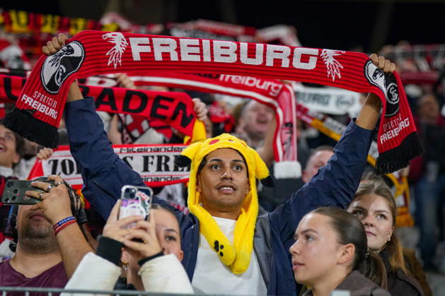 Deutschland: Fussball UEFA Conference League 2026 - 2027, 1. Spieltag - SC Freiburg vs FK Jablonec - Europa-Park-Stadion (Freiburg): Fan des SC Freiburg mit gelber Pikachu-Mütze hält einen rot-schwarzen Fanschal mit der Aufschrift FREIBURG und Vereinswappen über den Kopf. Porträt eines Anhängers auf der Tribüne des Europa-Park-Stadions beim UEFA Conference League-Spiel gegen FK Jablonec. SC Freiburg, Fussball, Europapokal, Fans, Zuschauer, Fankultur, Fanschal, Fanartikel, Merchandising, Pikachu, Pokà mon, Kostüm, Verkleidung, Vereinsfarben, Heimfans, Stimmung, Begeisterung, Supporter, Smartphone, Stadion. Copyright: xJOERANxSTEINSIEKx