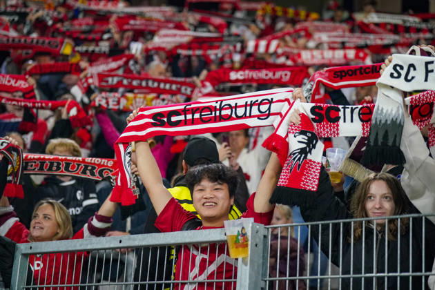 Deutschland: Fussball UEFA Conference League 2026 - 2027, 1. Spieltag - SC Freiburg vs FK Jablonec - Europa-Park-Stadion (Freiburg): Lächelnder Fan des SC Freiburg hält einen rot-weissen Fanschal mit der Aufschrift scfreiburg über den Kopf. Porträt eines begeisterten Anhängers auf der Tribüne des Europa-Park-Stadions beim UEFA Conference League-Spiel gegen FK Jablonec. SC Freiburg, FK Jablonec, Fussball, Europapokal, Fussballfan, Fans, Zuschauer, Fankultur, Fanschal, Vereinsfarben, Vereinswappen, Fanartikel, Merchandising, Emotionen, Begeisterung, Heimfans, Stadion, Tribüne, Supporter, Fanblock. Copyright: xJOERANxSTEINSIEKx