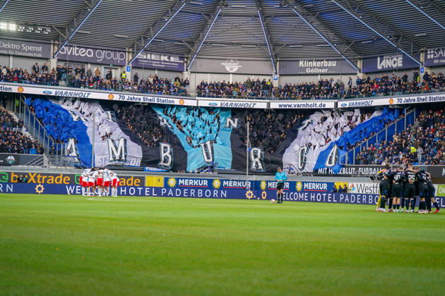Deutschland: Fussball Bundesliga 2026 - 2027, 7. Spieltag - SC Paderborn vs Hamburger SV - Home-Deluxe-Arena (Paderborn): Innenansicht der Home-Deluxe-Arena in Paderborn mit grosser blau-schwarz-weisser Choreographie der Heimfans des SC Paderborn 07, Schriftzug HAMBURG. Fans, Ultras, Fanchoreo, Fanszene, Fahnen, Zuschauer, Tribüne, Fanblock, Stimmung, Mannschaftskreise von SC Paderborn und Hamburger SV vor Spielbeginn, Fussball, Bundesliga, Stadion, Sportstätte, Totale, Spielfeld, Schiedsrichter, Flutlicht, Werbung, Sponsoren, Werbebanden, Merkur, buXtrade, Varnholt, Welcome Hotel. Copyright: xJOERANxSTEINSIEKx