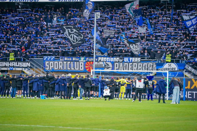 Deutschland: Fussball Bundesliga 2026 - 2027, 7. Spieltag - SC Paderborn vs Hamburger SV - Home-Deluxe-Arena (Paderborn): Heimsieg des SC Paderborn 07 gegen den Hamburger SV (HSV). Spieler, Trainer und Betreuer feiern nach Spielende gemeinsam mit den Heimfans vor der Fankurve der Home-Deluxe-Arena. Siegesfeier, Jubel, Mannschaft, Mannschaftsfoto von hinten, Schulterschluss, Fans, Ultras, Zuschauer, Tribüne, Fahnen, Schals, Fangesänge, Emotionen, Bundesliga, Fussball, Heimsieg, Sportstätte, Innenansicht, Totale, Hintertorperspektive, Tor, Fanbanner, Fankultur, Zusammenhalt. Copyright: xJOERANxSTEINSIEKx