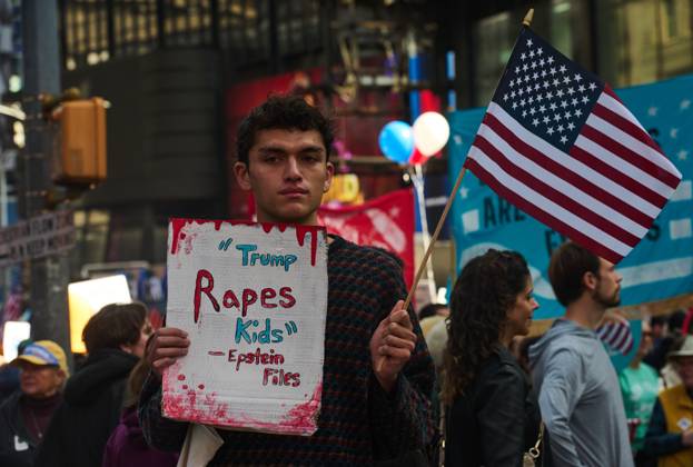 October 18, 2025, New York, New York, USA: A protester holds an American flag and a sign that reads, â€oeTrump Rapes Kids - Epstein Files†at the New York City No Kings protest. New York USA - ZUMAl171 20251018_znp_l171_039 Copyright: xEdnaxLeshowitzx
