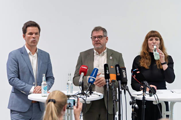 Berlin, 08.10.2026: Werner Graf (Bündnis 90 Die Grünen, M.) spricht neben Steffen Krach (SPD, l.) beim gemeinsamen Pressestatement nach Abschluss der Vorgespräche ihrer Parteien im Foyer des Hauses der Statistik, Kerstin Wolter-Ehling (Die Linke, r.) trinkt aus einer Wasserflasche. Pressestatement von Linke, Grünen und SPD in Berlin
