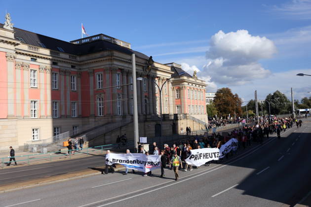 Demonstranten laufen mit Bannern Brandenburg Prüf! sowie Prüf heute. Schütz morgen! am Landtag während einer Demonstration für die Überprüfung rechtsextremer Parteien durch das Bundesverfassungsgericht, Potsdam, 10. Oktober 2026. Prüf-Demo in Potsdam