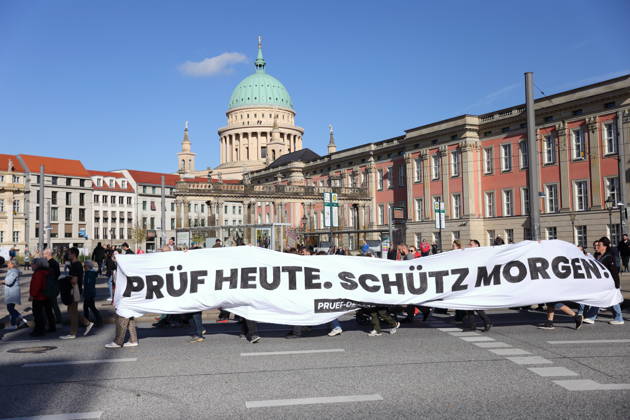 Demonstranten laufen mit Banner Prüf heute. Schütz morgen! am Landtag während einer Demonstration für die Überprüfung rechtsextremer Parteien durch das Bundesverfassungsgericht, Potsdam, 10. Oktober 2026. Prüf-Demo in Potsdam