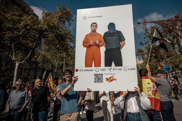 October 12, 2026, Barcelona, Catalonia, Spain: A demonstrator carries a placard styled as a social media post depicting Spanish Prime Minister Pedro SoÂ¡nchez in an orange prison uniform during a rally marking SpainÃ¢â‚¬â ¢s National Day. Barcelona Spain - ZUMAo105 20261012_fap_o105_009 Copyright: xMatthiasxOesterlex