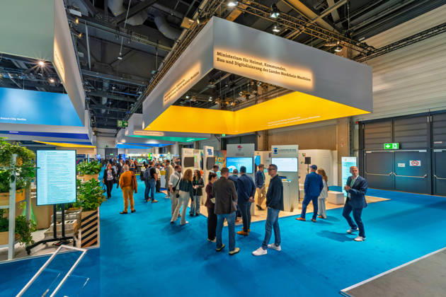 Berlin, 13.10.2026: Besucher am Stand des Ministeriums für Heimat, Kommunales, Bau und Digitalisierung des Landes Nordrhein-Westfalen auf der Smart Country Convention; links ist der Stand von Smart City Berlin zu sehen, im Hintergrund der des Landkreistags. Zahlreiche Bundesländer, Städte und kommunale Spitzenverbände präsentieren auf der Messe ihre Projekte zur digitalen Verwaltung. Die Smart Country Convention (SCCON) ist die Kongressmesse für die Digitalisierung des öffentlichen Sektors und wird vom Digitalverband Bitkom gemeinsam mit der Messe Berlin veranstaltet. Vom 13. bis 15. Oktober 2026 treffen sich auf dem Berliner Messegelände Vertreter aus Bund, Ländern und Kommunen mit Unternehmen der Digitalwirtschaft, um über digit