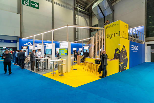 Berlin, 13.10.2026: Der gelb gestaltete Stand des Landes Baden-Württemberg unter der Digitalmarke digital.LÄND auf der Smart Country Convention, daneben der Stand der Initiative EGOVC und der Metropolregion Rhein-Neckar. Mit der Marke digital.LÄND bündelt das Land seine Projekte zur Digitalisierung von Verwaltung, Wirtschaft und Gesellschaft. Die Smart Country Convention (SCCON) ist die Kongressmesse für die Digitalisierung des öffentlichen Sektors und wird vom Digitalverband Bitkom gemeinsam mit der Messe Berlin veranstaltet. Vom 13. bis 15. Oktober 2026 treffen sich auf dem Berliner Messegelände Vertreter aus Bund, Ländern und Kommunen mit Unternehmen der Digitalwirtschaft, um über digitale Verwaltung, Smart City und digita
