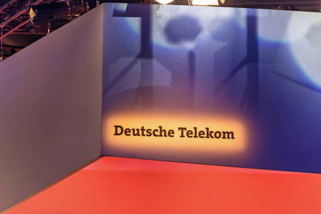 Berlin, 13.10.2026: Der beleuchtete Schriftzug Deutsche Telekom an einem Deckenaufbau über dem Messestand des Konzerns auf der Smart Country Convention in der Halle hub27. Die Telekom präsentiert dort Lösungen für die öffentliche Verwaltung, darunter KI-Agenten, souveräne Cloud-Angebote und einsatzkritische Kommunikation. Die Smart Country Convention (SCCON) ist die Kongressmesse für die Digitalisierung des öffentlichen Sektors und wird vom Digitalverband Bitkom gemeinsam mit der Messe Berlin veranstaltet. Vom 13. bis 15. Oktober 2026 treffen sich in der Halle hub27 Vertreter aus Bund, Ländern und Kommunen mit Unternehmen der Digitalwirtschaft, um über digitale Verwaltung, Smart City und digitale Souveränität zu diskutiere