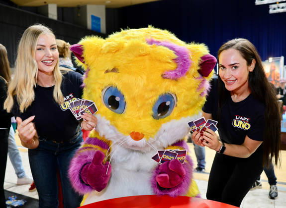 Spiel 26 Messe in Essen - Mattel stellt Neuheit UNO LIAR S Kartenspiel vor - die Models Lydia und Sorin mit Spiel-Maskottchen MEEPS Essen Grugahalle Messe NRW Deutschland