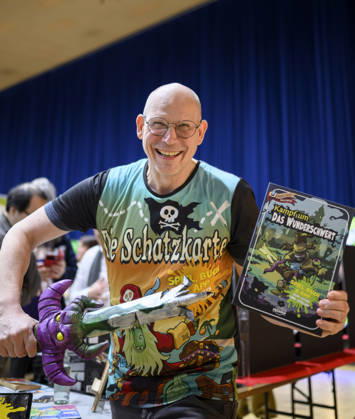 Ein Mitarbeiter präsentiert das Spiel - Kampf um das Wunderschwert - von Peasoup (Dänemark), 3-in-1 Spiel, Gamebook, Brettspiel und interaktive App in einem, Neuheitenschau, am 21.10.2026 Messe SPIEL Essen vom 22.10 - 25.10.2026 in E s s e n Deutschland. Grugahalle