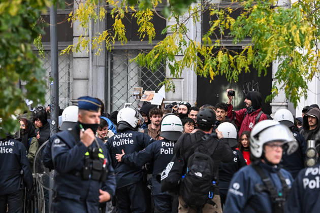 Riot police officers in protective gear surround a group of demonstrators, some wearing face coverings and others unmasked, during student protests in central Brussels, Belgium, on 24 October 2026. Several people film the police operation with their mobile phones as officers confront the protesters amid unrest in the city centre.